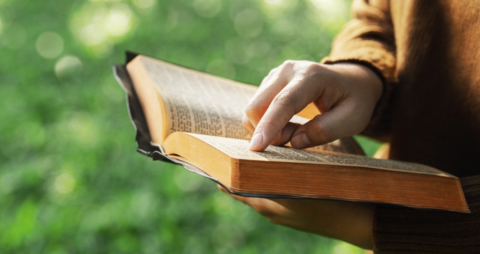 The concept of reading the Bible and praying for God’s blessings. Therapeutic living in peace with nature while spending time with God. Young woman’s hand pointing to a Bible topic